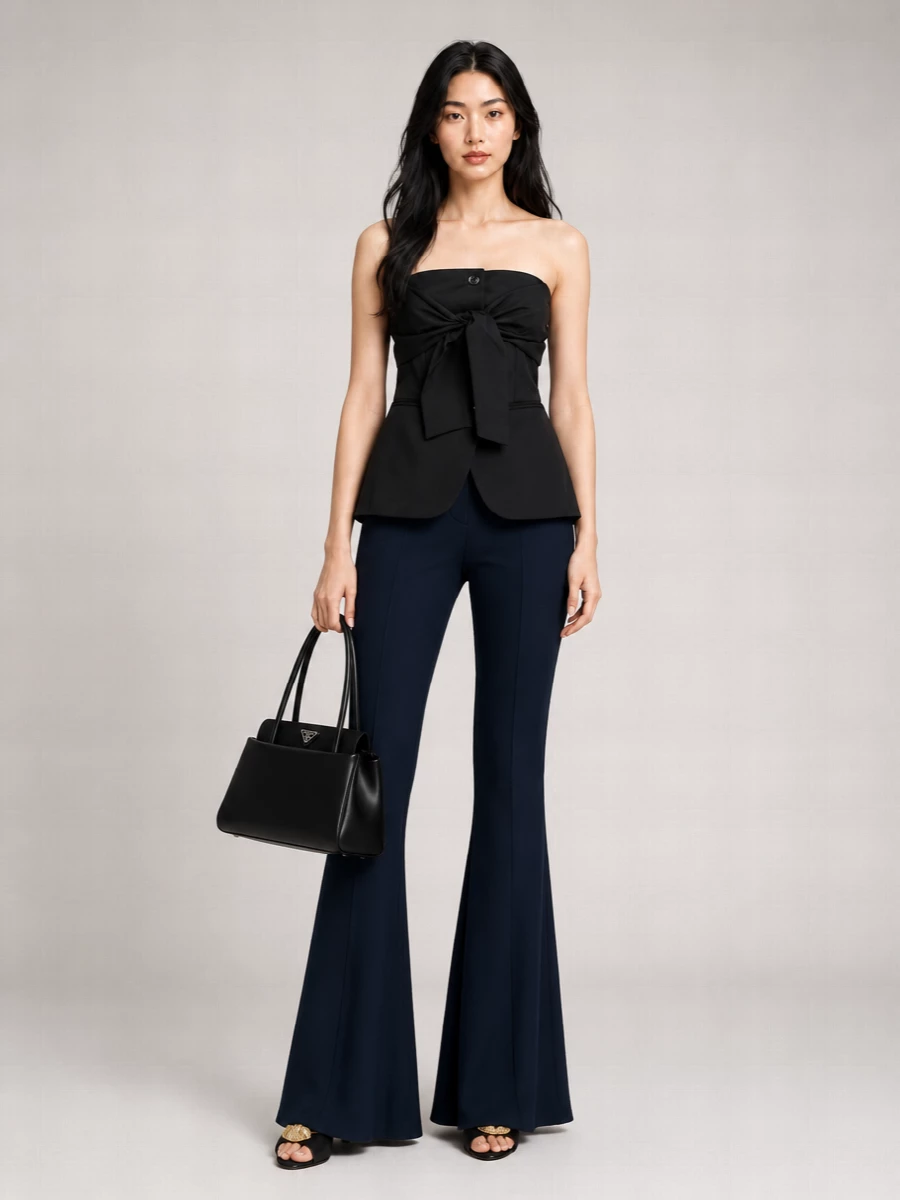 Deep navy flared trousers meet a sculpted strapless peplum for a quietly commanding take on evening suiting. A cummerbund-style belt carves out the waist, while black stiletto mules and a structured Prada top-handle keep the palette sharp, monochrome and precise. The result is a long, lean silhouette that feels tailored, sensual and unmistakably modern for night.”