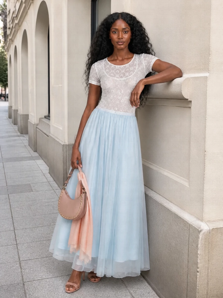 A sheer Marine Serre tee sits over a floaty ice-blue maxi, mixing moonlit motifs with gauzy movement in a soft, romantic palette. Blush stilettos and a curved Valentino shoulder bag sharpen the mood into something distinctly night-out but still delicate. A whisper-light blush stole finishes the set with just enough color to bridge the pale tones without stealing focus from the transparency play.