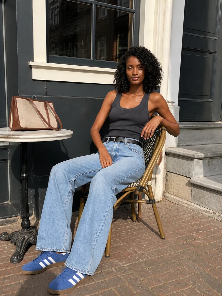 Light Haikure wide-leg denim is anchored with a charcoal ribbed tank and a clean black belt, keeping the palette cool and minimal. Dusty blue Adidas sneakers pick up the washed tones without competing, while the structured Hereu shoulder bag in oatmeal and chocolate adds a quiet hit of texture and polish. The result feels relaxed and modern, with long, easy lines that work from coffee runs to casual dinners.