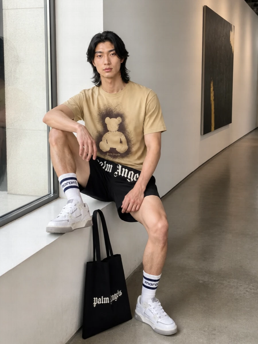 A sand teddy tee meets sharp black logo shorts for a clean, logo-driven streetwear uniform that feels easy but intentional. Off-white skate sneakers and striped socks pick up the tee’s warmth and keep everything light on the eye. The black Palm Angels tote locks in the monochrome accents, so the teddy graphic stays the central punch of attitude.