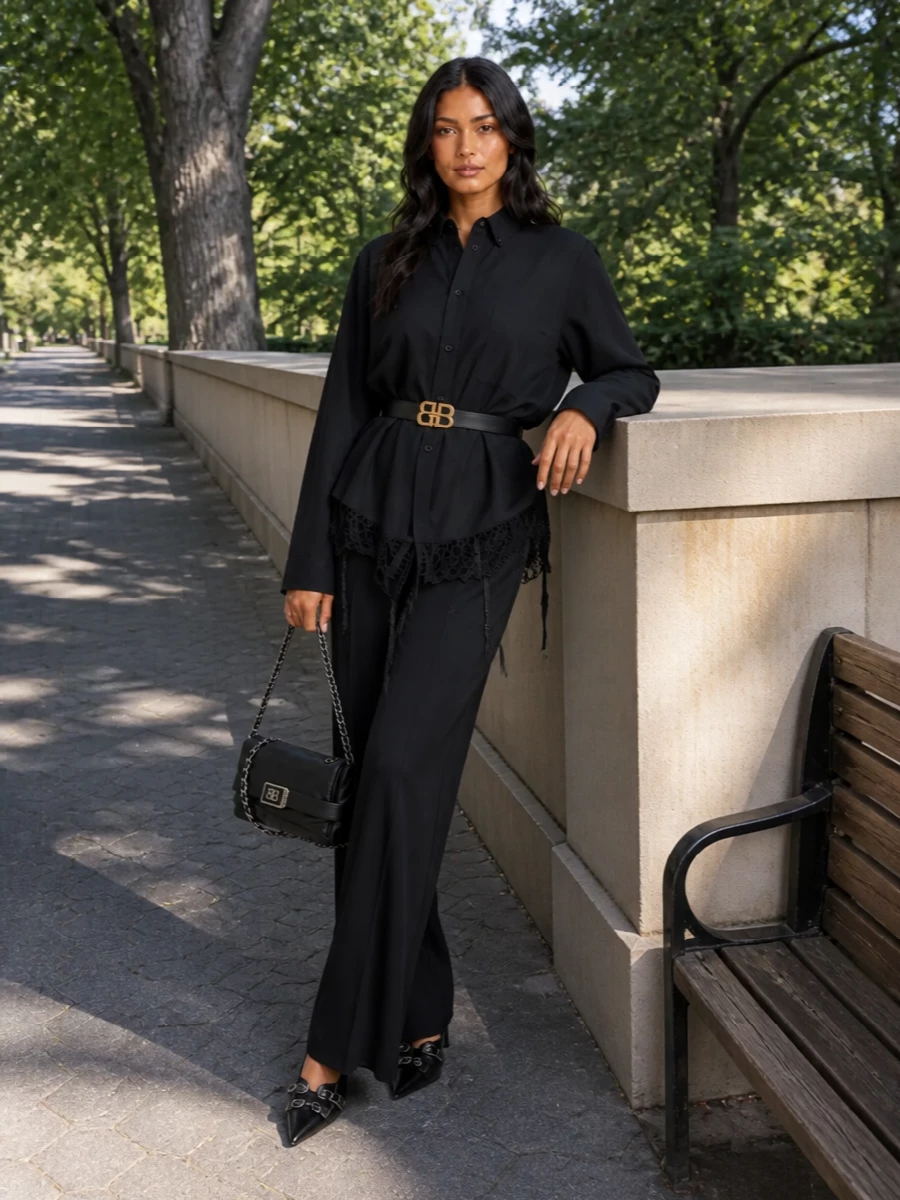 Balenciaga’s lace-hem shirt falls over high-waisted, fluid wide-leg trousers for a long, inky column that feels romantic and sharply urban at once. Pointed buckle-detailed pumps and a silver-chain BB bag extend the hardware story, turning the softness of the lace into something distinctly after dark. The result is a monochrome, runway-leaning outfit that reads tailored from a distance but reveals subversive detailing up close.