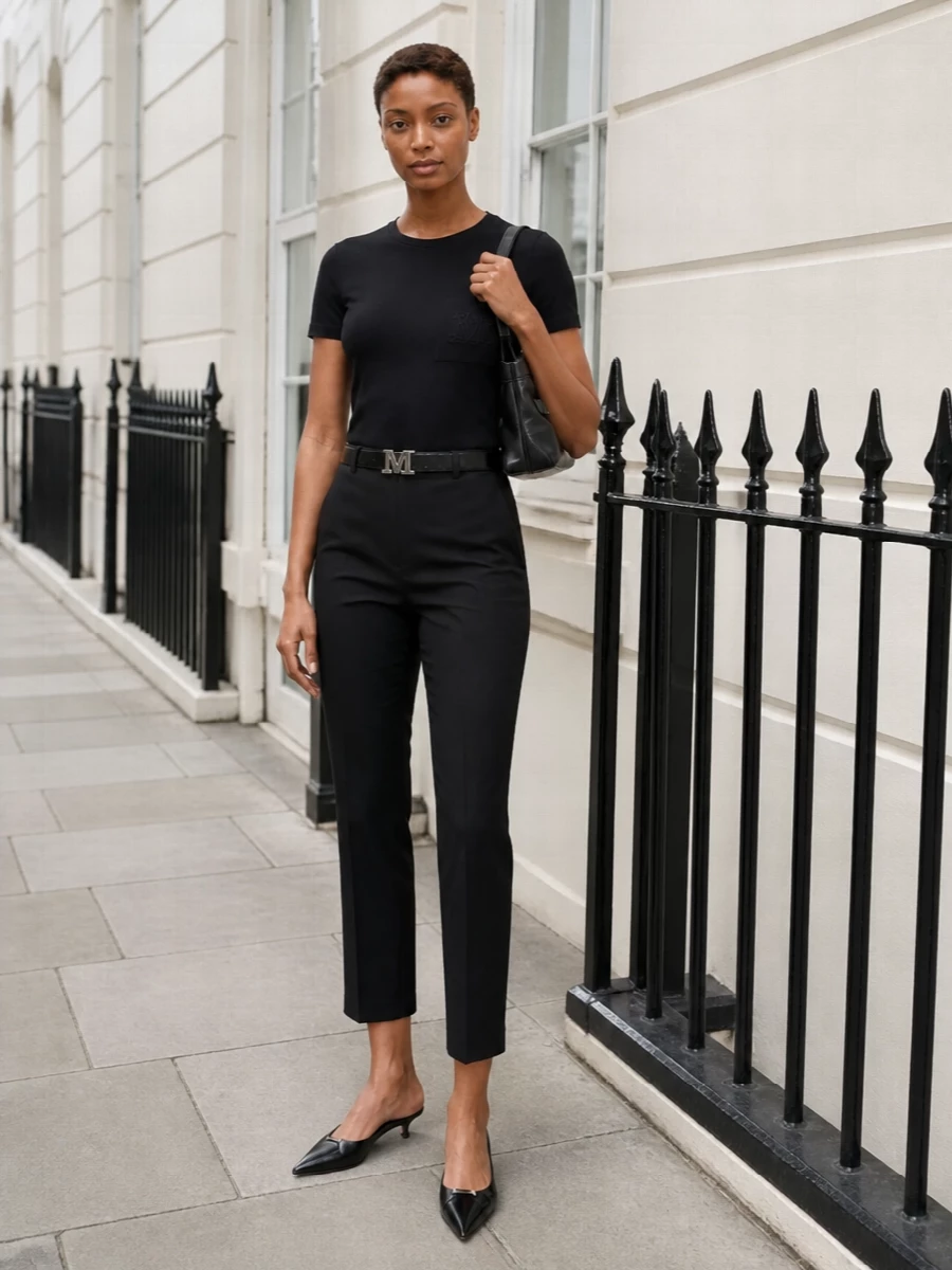 A black Max Mara tee meets high-waisted cropped tailoring for a precise, city-ready column in pure monochrome. The pointed kitten heel and structured top-handle bag introduce just enough formality, while the slim belt quietly sharpens the waist. It is a minimalist uniform that moves easily from focused workdays to low-key dinners without changing a piece.