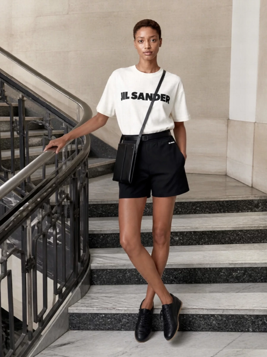 A crisp off-white logo tee sits against clean black sport shorts for a graphic, Jil Sander take on off-duty dressing. Streamlined black sneakers and a slim leather cross-body keep the lines neat and urban, with the optional narrow belt there if you want a slightly more defined waist without losing ease.