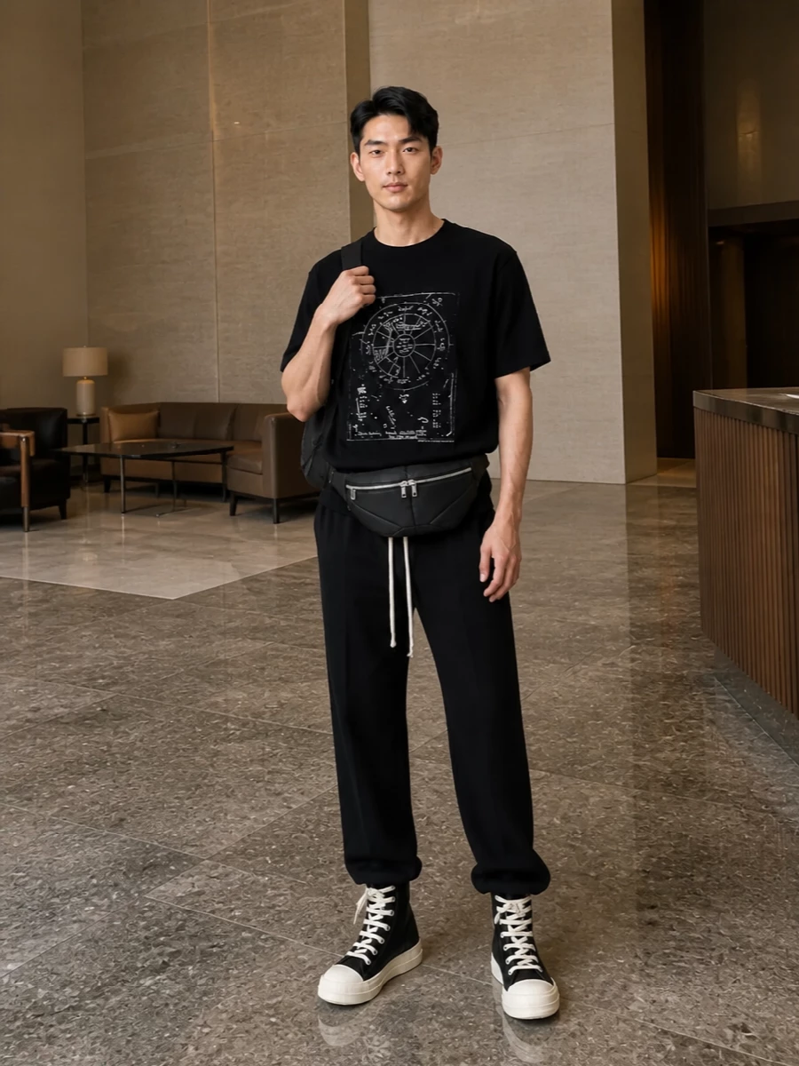 A stark black and off-white palette lets the astrological graphic stay the focal point, grounded by straight-leg drawstring trousers that echo the tee’s relaxed line. Chunky high-top sneakers and a padded belt bag add structured volume at the feet and waist, keeping the proportions long and vertical. The result is a clean, cerebral streetwear uniform that reads unmistakably Rick without feeling costume-y.