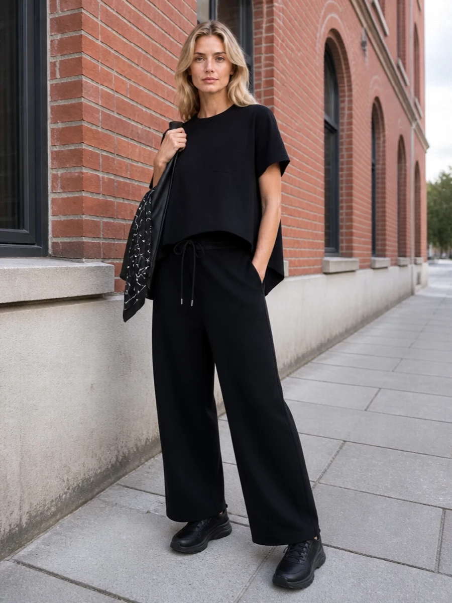 Monochrome and architectural, this pairing lets the asymmetric tee and fluid wide leg do all the work, reading relaxed yet sharply considered. All-black sneakers keep the line clean and grounded, while the triangular bag and sketch-print scarf echo the outfit’s sculptural, slightly conceptual attitude without breaking the quiet palette.