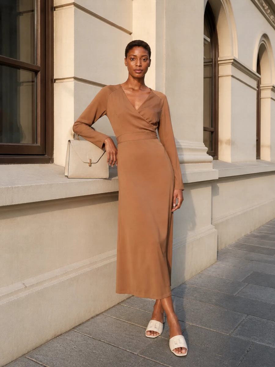 The camel satin wrap dress with the structured ivory Valextra bag creates a calm, tonal story that feels formal without ever looking severe. Choosing the dress route rather than separates keeps the silhouette long and unbroken, which suits the bag’s architectural top-handle shape. Ivory block-heel slides pick up the bag’s tone and keep the finish minimalist, refined and easy for long city evenings or polished dinners.