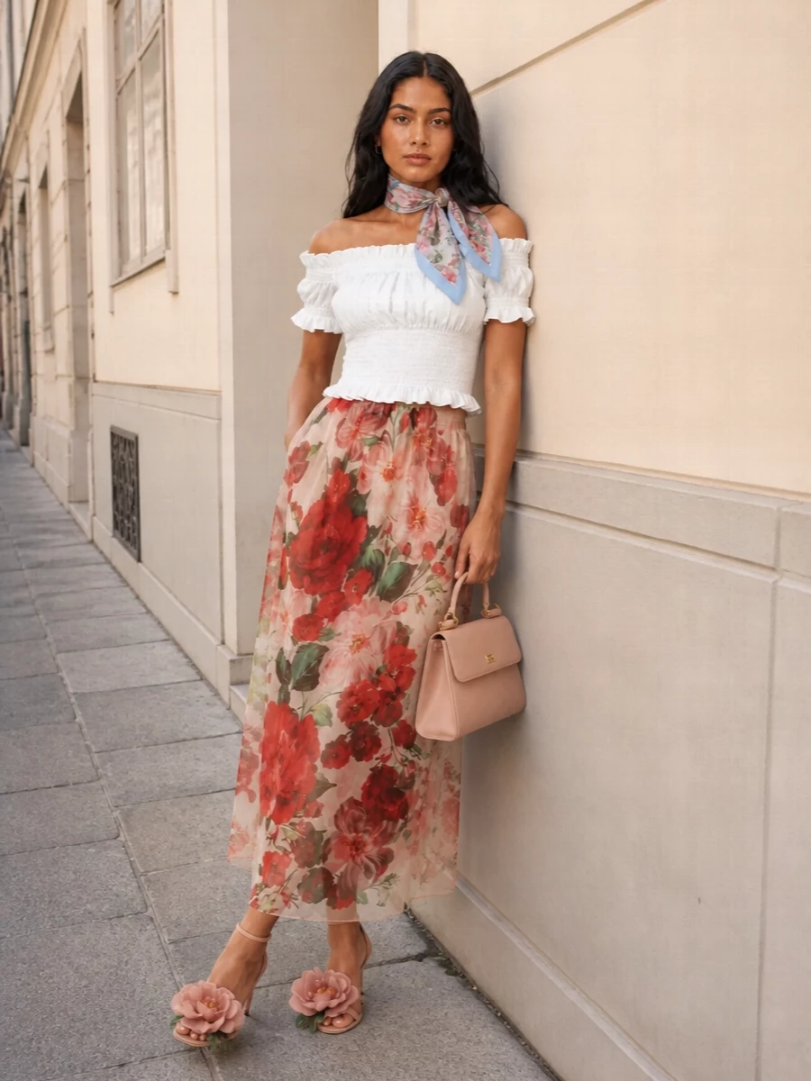 A sheer rose garden of a skirt is grounded with a crisp white off-shoulder top for romance that still feels light and modern. Blush rose-detailed stilettos and a structured blush top-handle keep the palette soft and elongating, perfect for sunlit terraces or summer evenings. A silk scarf in blush and sky blue is the final, easy gesture of Sicilian glamour, whether in your hair or knotted to your bag.