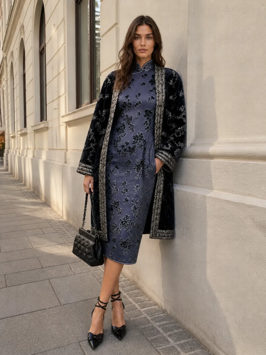 This pairing leans into a moody, romantic evening mood by echoing the coat’s inky florals and silver jacquard with a slate blue velvet-sheathed dress beneath. Opting for the dress path keeps the lines long and uncluttered, letting the cape-coat act as a dramatic outer layer rather than fighting another top-and-bottom print story. Crystal-detailed slingbacks and a minimal quilted shoulder bag bring just enough sparkle to meet the coat’s opulence while maintaining a polished, quiet-luxury attitude.