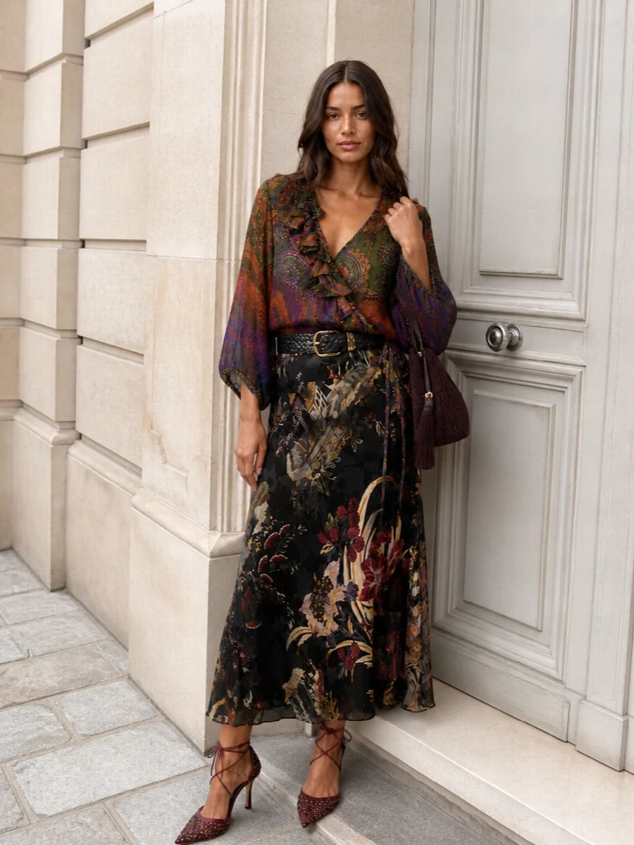 Romantic Etro paisleys in deep greens, plums and burnished tones play against a dark, flared midi to create a fluid, print-on-print statement that still feels composed. A bordeaux stiletto and burgundy tasselled bag sharpen the mood into evening, while a braided black and gold waist defines the silhouette so all that movement reads intentional rather than busy. The result is bohemian, opulent and ready for terraces, openings and intimate dinners once the light drops.