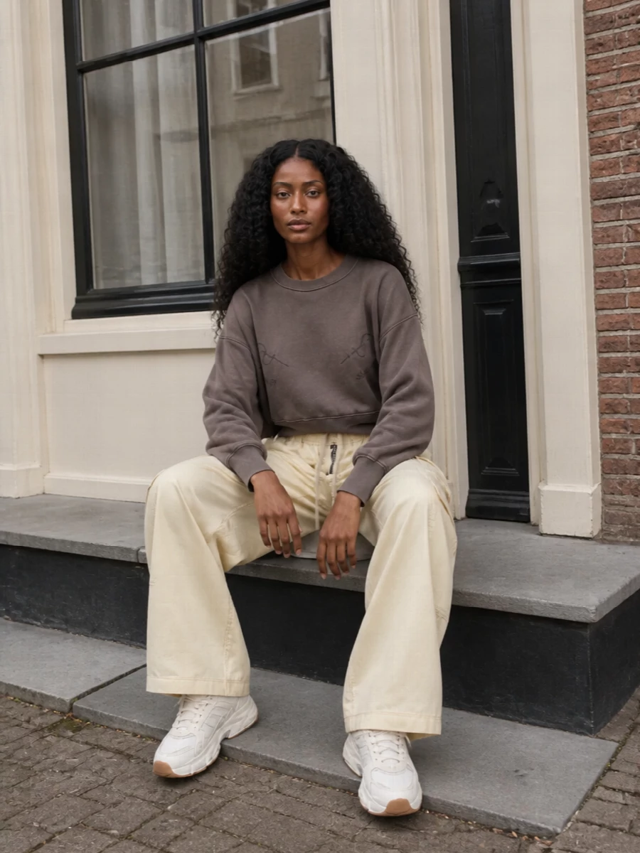 Soft neutrals and easy volume keep this outfit grounded in modern streetwear, with the chunky runner echoed by wide buttercream cargos and a cropped taupe sweatshirt. The proportions stay relaxed but intentional, with the waist definition and long leg line preventing the pieces from feeling sloppy. A slim buttercream cross-body finishes it with just enough structure to move from coffee runs to low-key dinners in one go.
