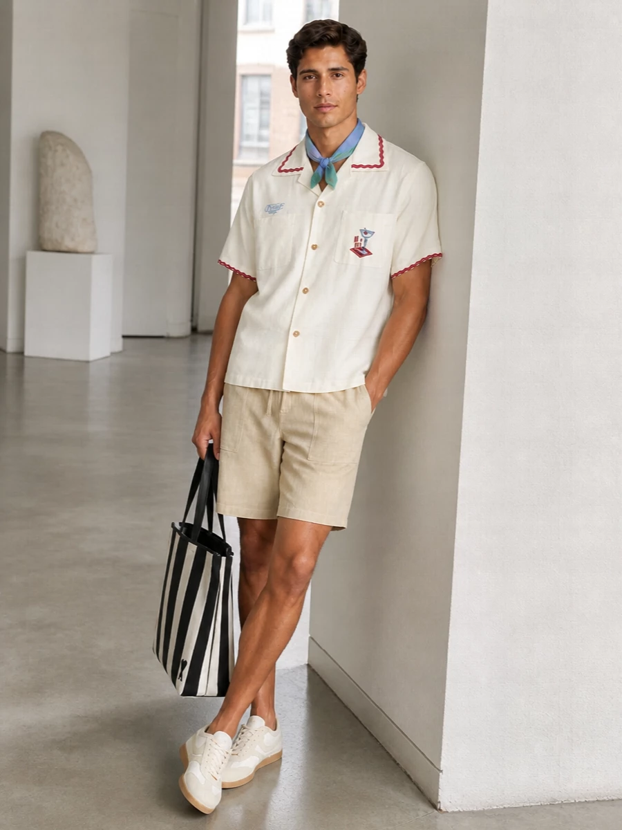 A Riviera-leaning camp shirt meets softly tailored beige shorts for a relaxed, preppy summer uniform that feels easy but considered. Off white retro runners keep everything light on the eye and genuinely walkable, while a bold striped tote and a touch of blue-green at the neck finish it with confident, coastal personality.