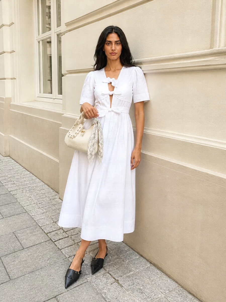 A crisp white Ganni midi is grounded with sleek black slingback flats for a clean, city-ready take on summer romance. The ivory bucket bag keeps the palette light, while a delicate monochrome scarf adds just enough texture and interest without crowding the cut-out bodice. It is an easy warm-weather outfit that moves smoothly from daytime wandering to a relaxed dinner reservation.