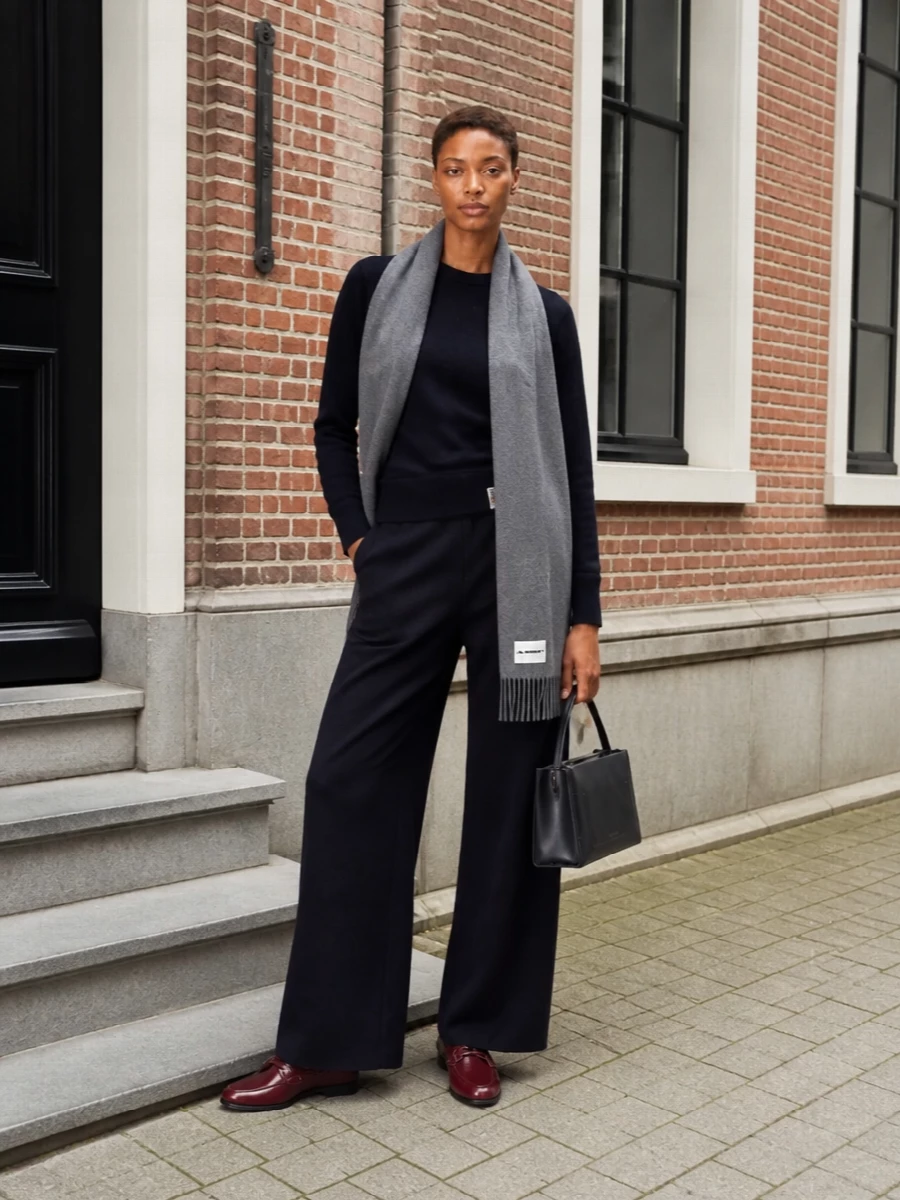 Deep navy knitwear and wide-leg trousers create a clean, elongated line that feels composed yet relaxed. Oxblood loafers and an inky structured bag bring just enough contrast and polish. A heather-grey scarf softens the palette and reinforces the understated, quietly luxurious mood.