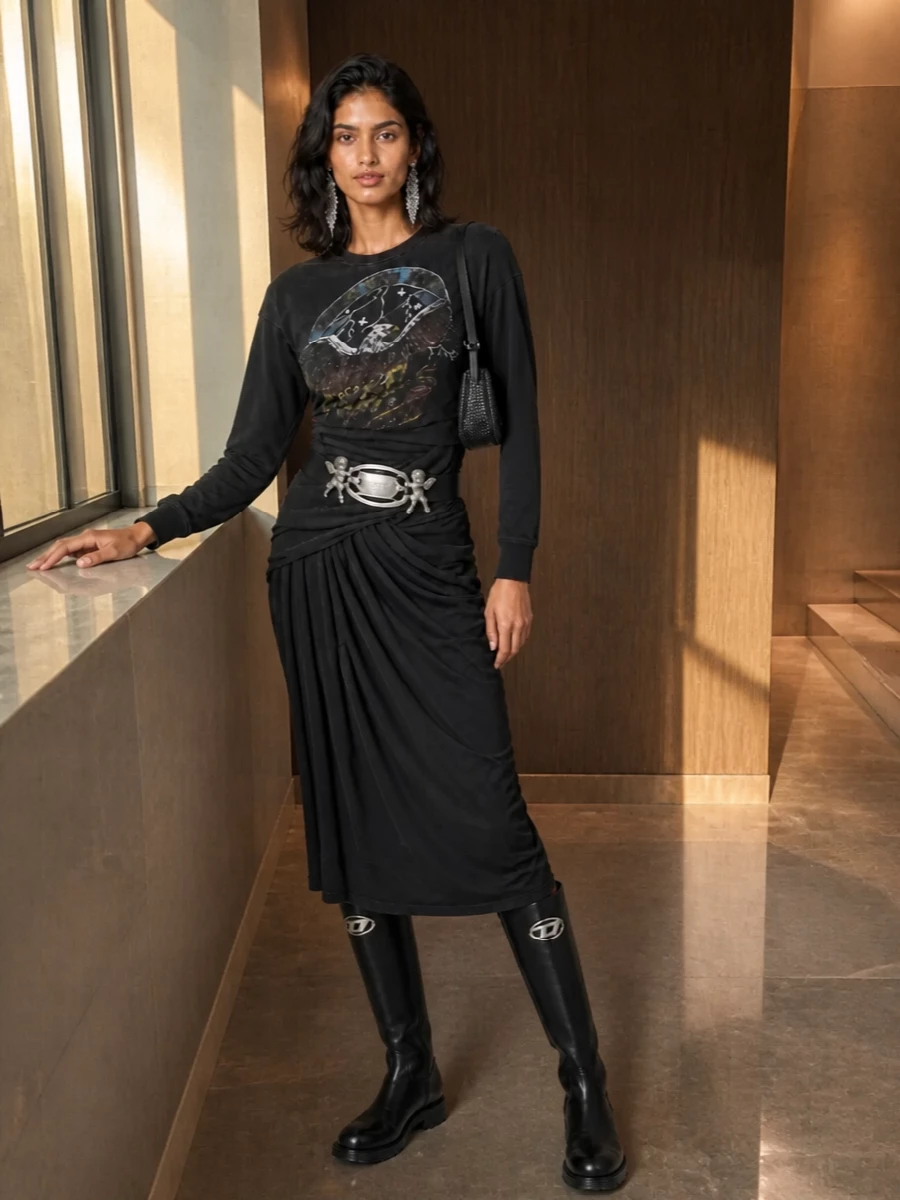 A ruched Diesel sweatshirt dress meets solid black knee-high boots for a night-ready streetwear take that feels tough but still body conscious. Charcoal rhinestone denim at the shoulder and liquid silver at the ears keep the energy club-facing while staying in the same grungy palette. A cherub-buckle belt is the irreverent detail that ties the hardware story together without fighting the graphics.