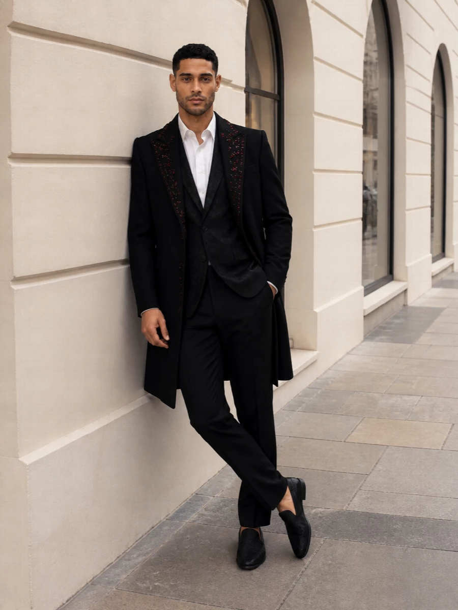 A pitch-black column of tailoring lets the garnet-trimmed coat take center stage, with tonal jacquard and brocade adding depth only up close. Slim trousers and discreet evening accessories keep the silhouette long, sharp and nightclub-ready without tipping into costume.