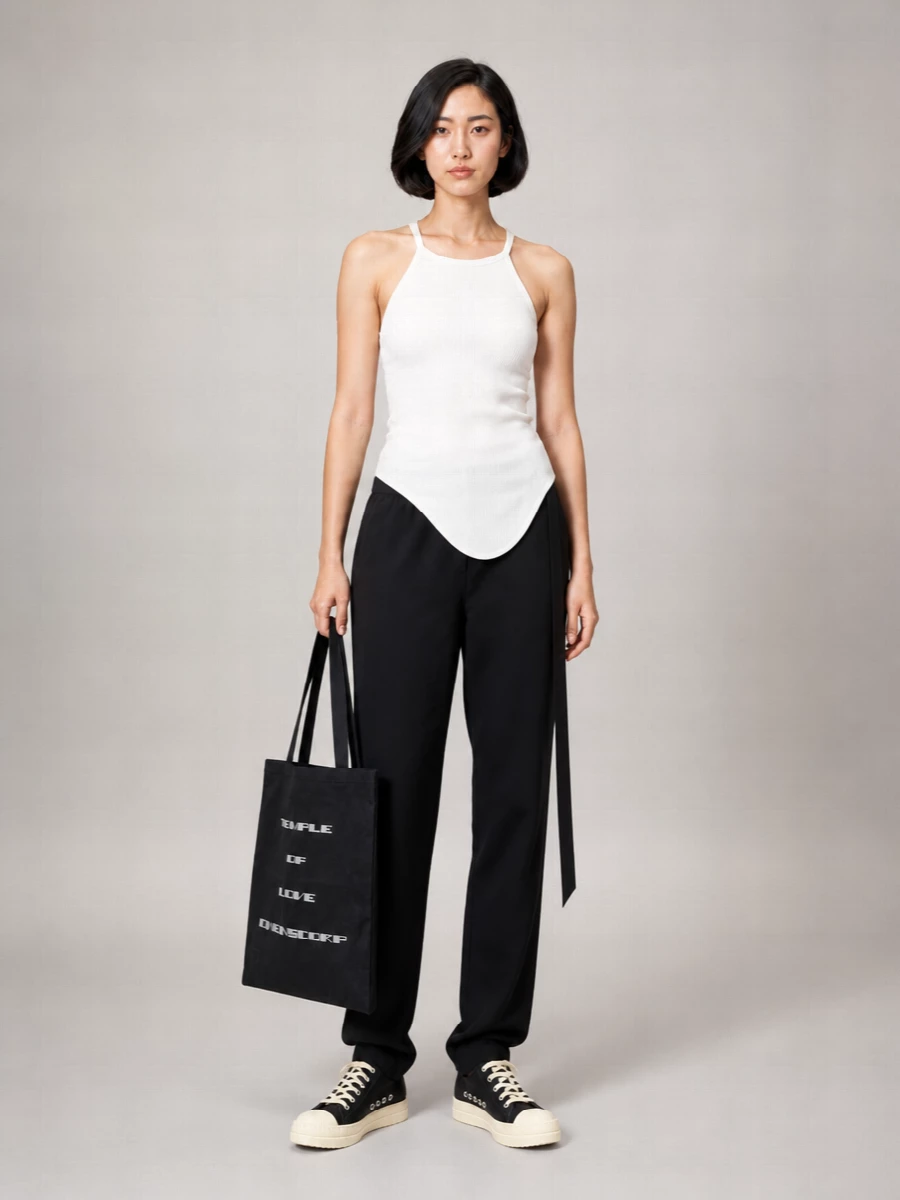 A dark, elongated base of relaxed black trouser and asymmetric slim tank keeps everything firmly in the Rick universe, low-key but sharply considered. The graphic low-top sneakers and oversized text tote play with proportion at the ground and in hand, so the body stays clean while the edges feel quietly subversive. It is an off-duty city uniform that reads directional without needing any extra styling tricks.