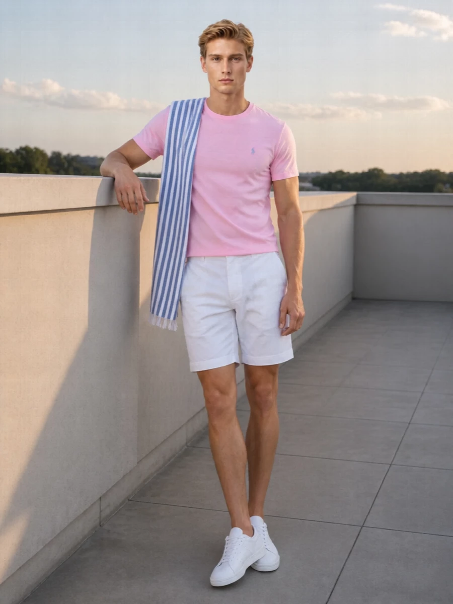 Soft pastel pink meets crisp white and clean sneakers for a fresh, collegiate summer uniform. The structured chino short keeps the mood neat, while the white leather court shoe and graphic dark tote stop the palette from feeling too sweet. A light striped scarf pulls the blues from the pony logo into the outfit, adding just enough detail to stay interesting and still relaxed.