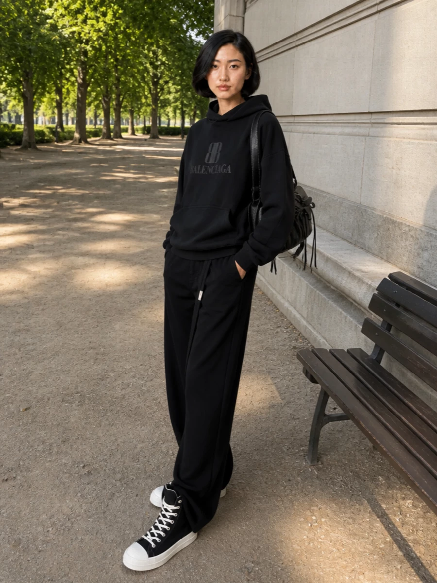 A black Balenciaga hoodie and fluid Ann Demeulemeester wide-leg trouser give the sneakers a clean, elongated frame, all in one monochrome story. The high waist and pooling hem work with the extended shaft of the shoe, so the volume reads intentional rather than bulky. Acne’s structured black shoulder bag finishes it with a subtle, utilitarian edge that still feels city ready.
