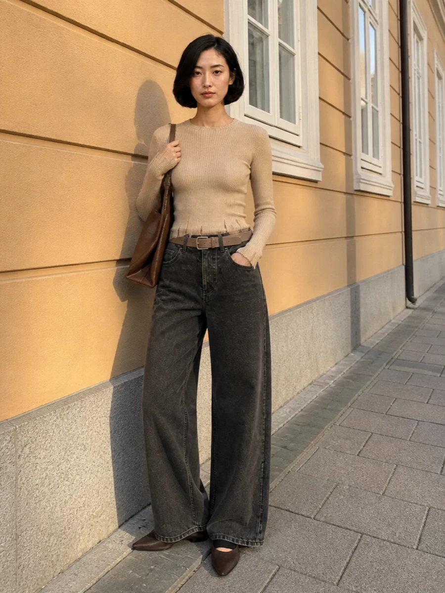 Washed charcoal wide legs meet a ribbed oatmeal knit for a calm, tonal play of texture that still feels relaxed. A pointed, low-profile flat and supple brown shoulder bag pull the line long and grounded, while a slim taupe belt gives just enough structure at the waist. It is an off-duty city uniform that reads thoughtful rather than styled.