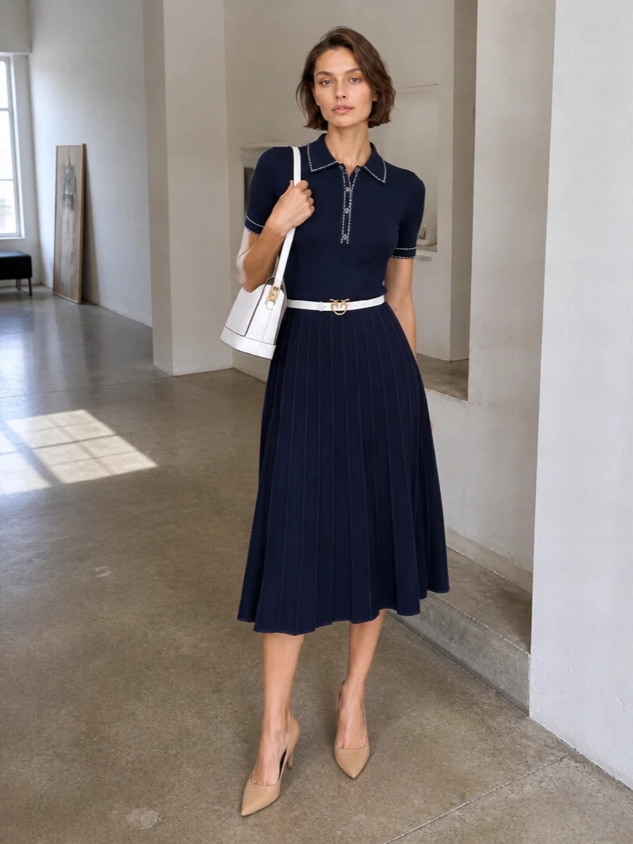 A navy knit midi goes smart and precise with nude heels and a white, edge-trimmed shoulder bag, keeping the palette clean and quietly collegiate. A slim white belt at the waist sharpens the polo collar and pleats, making this an easy choice for office days that move straight into dinner plans.