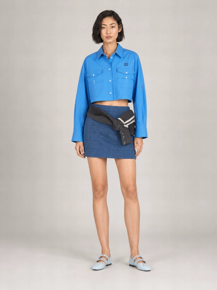 A sharp cobalt cropped shirt meets a checked denim mini for a preppy take on city dressing. Powder-blue Mary Janes and a collegiate knit cross-body keep the mood playful but polished, ideal for warm days when you still want structure.