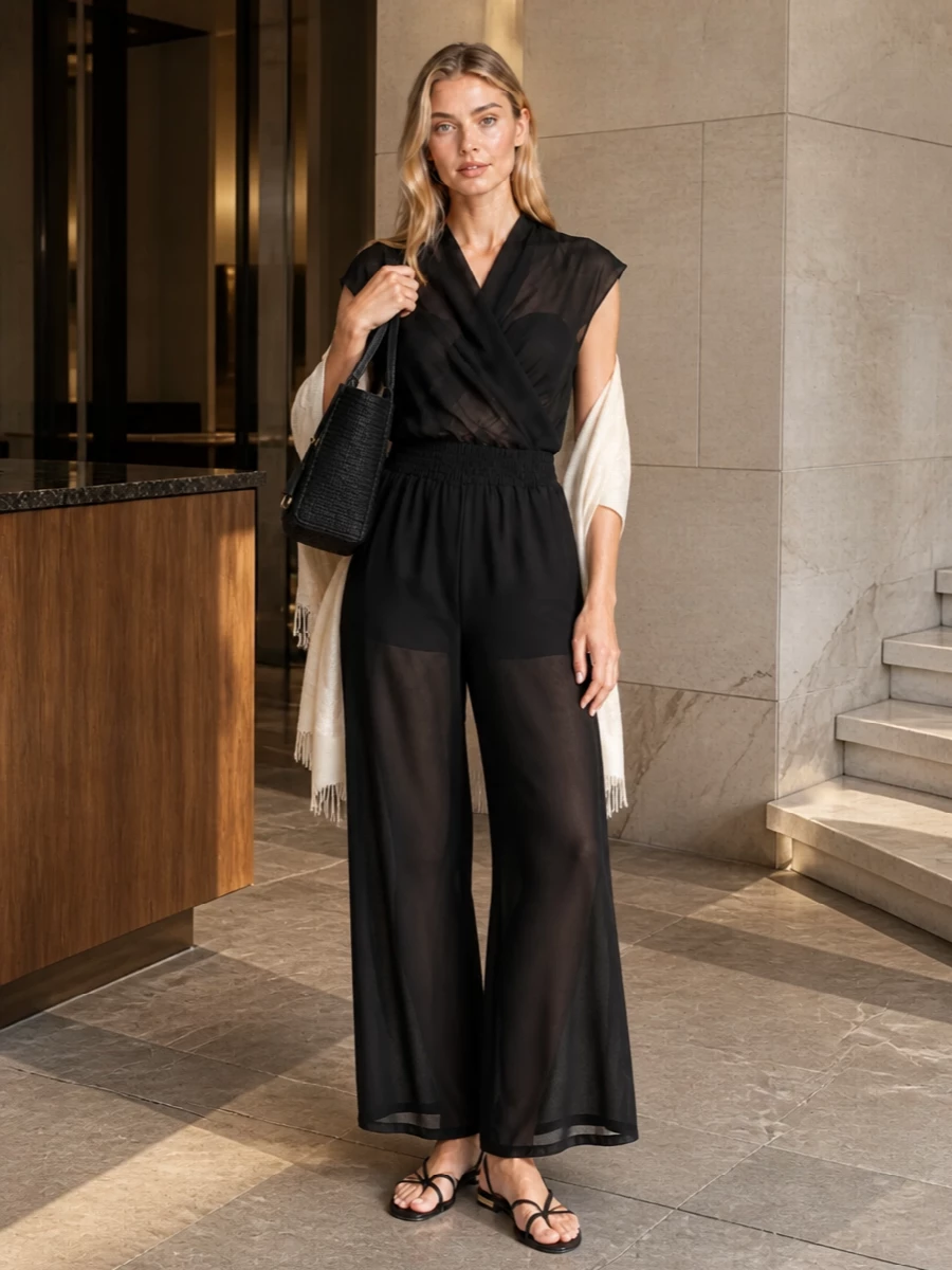 A sheer black jumpsuit meets barely-there flat slingbacks for a calm, after-sun mood that still reads polished enough for cocktails. The structured black raffia tote keeps it grounded and practical for poolside essentials. A soft neutral stole introduces just a trace of warmth and texture, so the whole outfit feels considered without losing its ease.