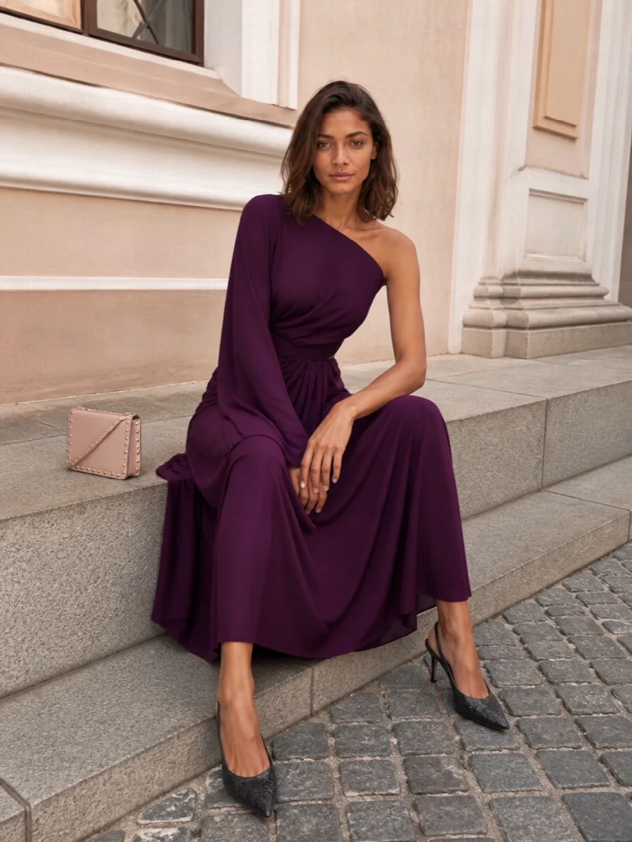 A statuesque deep-plum column paired with crystal-sheened black slingbacks lets the blush Rockstud clutch read as a soft, romantic accent rather than the main event. The asymmetric neckline and fluid draping keep the silhouette modern yet quietly glamorous, ideal for formal winter evenings where you want drama handled with restraint. Choosing the gown over separates preserves a clean line that flatters the bag’s structure and keeps the whole ensemble firmly in polished-cocktail territory.