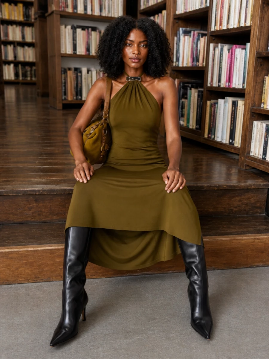 A fluid olive halter column dress and inky knee-high boots create a long, quiet line that feels modern and assured. The mustard suede shoulder bag slips into this palette like a warm accent, adding Parisian boho depth without disturbing the clean silhouette. Choosing the dress path keeps the outfit firmly in discreet evening territory, where the bag reads considered rather than casual.
