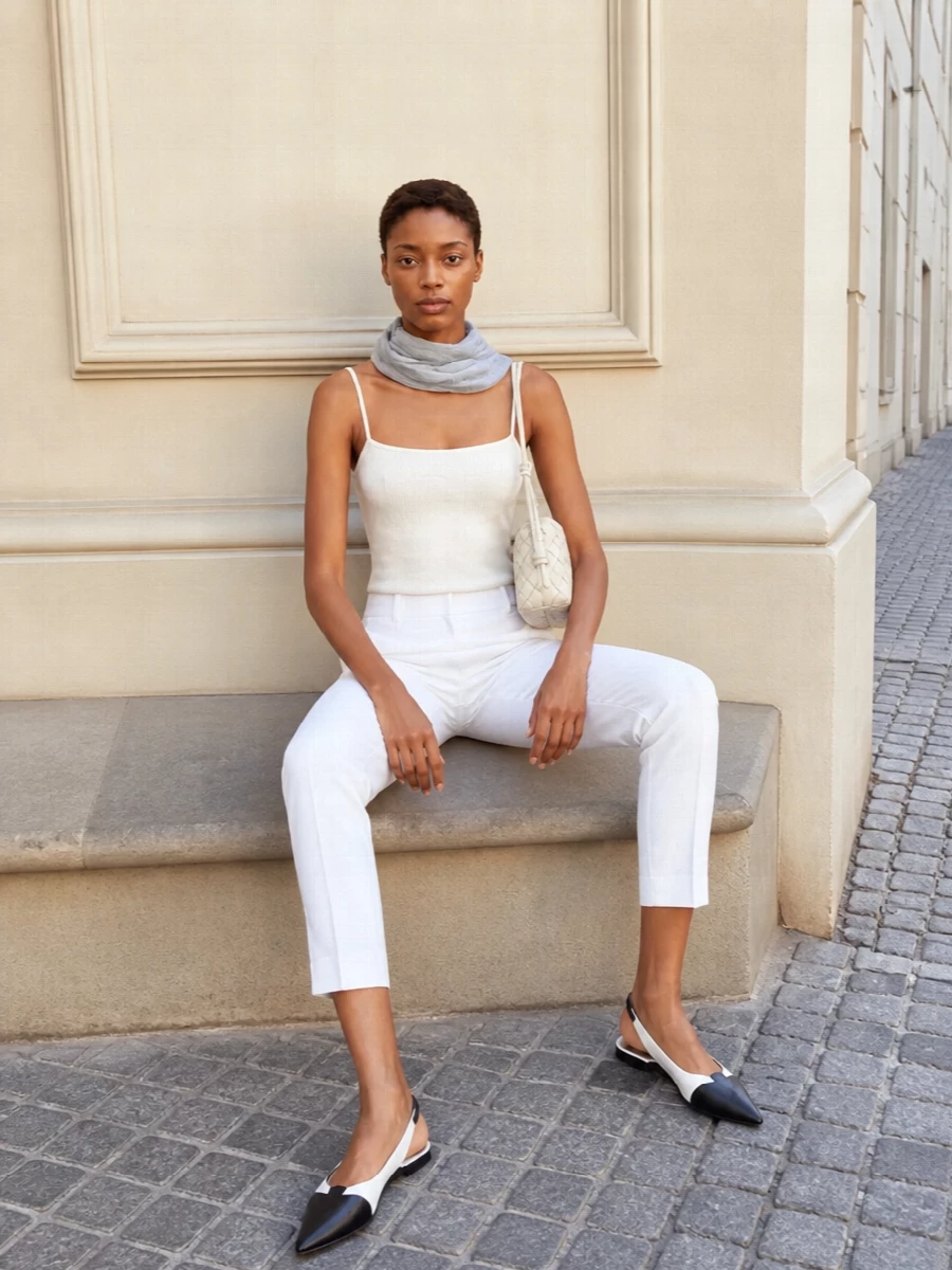 A soft-white bodysuit disappears into gallery-white tailored trousers for a calm, uninterrupted column of tone. Graphic black and white slingbacks ground the palette, while an ivory intrecciato bag and a whisper of dove-grey at the neck keep the mood precise but gentle. The result feels polished enough for the office yet relaxed enough for long, unhurried days in the city.
