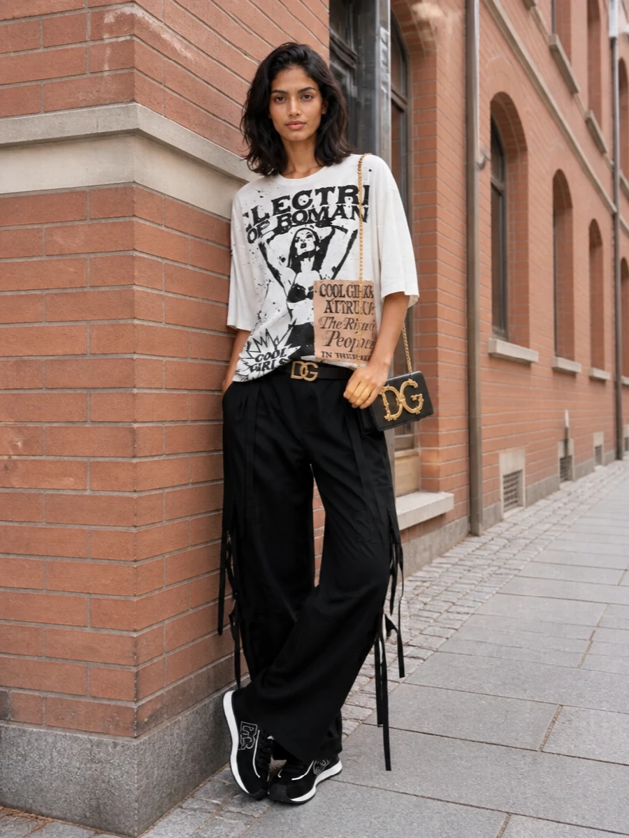 Dolce&Gabbana’s graphic tee drops over black cargo trousers for a low-key but high-impact club uniform built on volume and monochrome attitude. Logo runners keep it fast and grounded, while the baroque-chain mini bag and DG belt add just enough glam to read intentionally designer without losing the street edge.