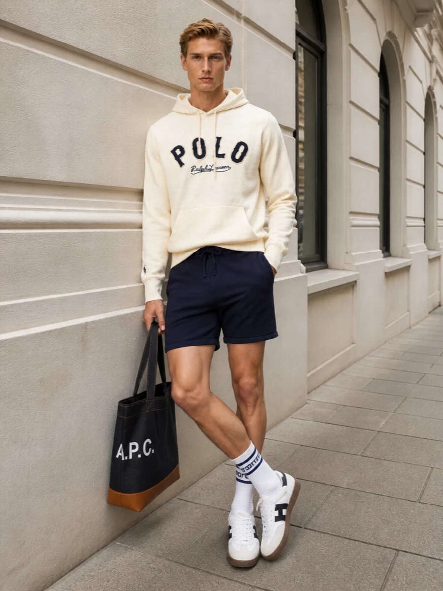 Cream and navy stay front and centre for a clean Polo-on-Polo story that feels sporty without reading gym-bound. Knit deck shorts keep the proportions neat and relaxed, while white Hogan sneakers and a structured denim tote sharpen the city-ready edge. Striped socks quietly reinforce the collegiate palette without stealing focus from the varsity chest logo.
