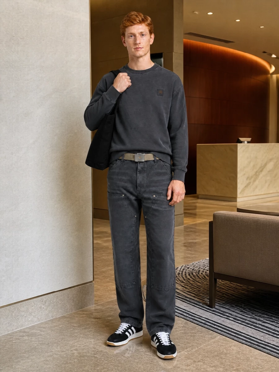 Charcoal work pants meet a washed charcoal crewneck for a monochrome take on utility that feels low-key and skate-driven. Black and white terrace sneakers tighten the streetwear edge, while a black tote and sand webbing belt keep the palette grounded and practical for long city days.