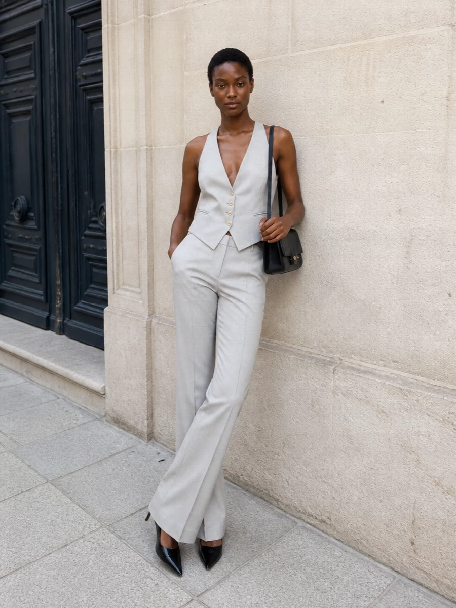 This look builds a modern three-piece tux in pale grey, pairing the high-rise flared trousers with the matching halterneck vest for a sculpted, elongated silhouette. Black patent stilettos and a slim black shoulder bag sharpen the palette, keeping the mood quietly opulent and impeccably tailored for FW evening dressing. The result is precise, sensual and powerfully minimal, with every element reinforcing the clean Tom Ford suiting line.