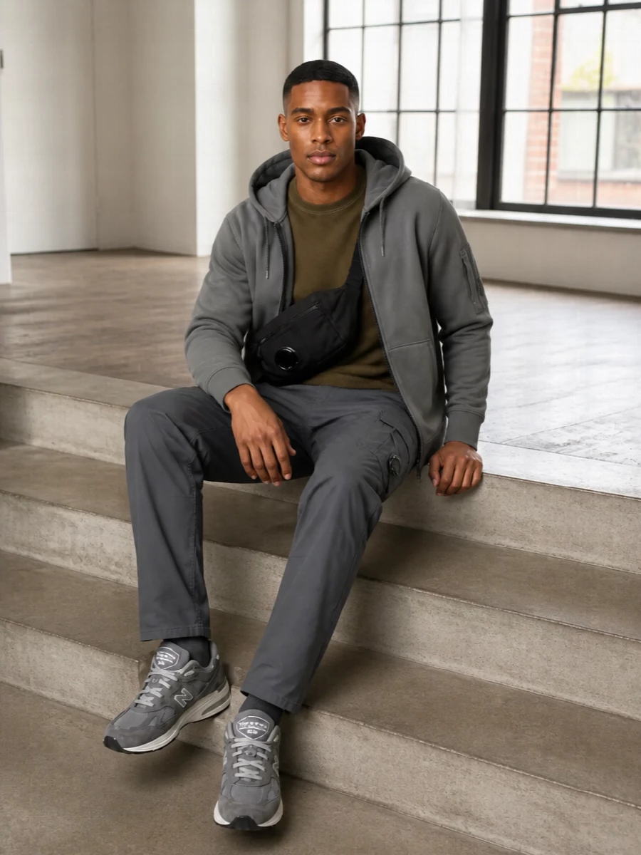 This is a tonal CP Company city uniform built around slate utility and soft technical fabrics. Olive on top warms the grey cargos and jacket, while grey New Balance runners keep everything quietly athletic. The compact black crossbody finishes it with just enough hardware and logo to feel considered without shouting.