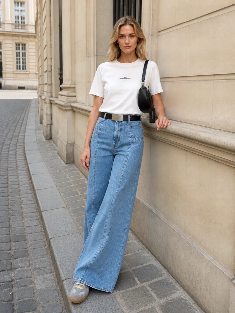 A crisp Margiela tee meets high-rise ultra-wide denim for a clean column that feels casual but decisively designed. Grey trainers keep it grounded and easy, while a curved black shoulder bag and slim logo belt add just enough structure and signal without breaking the quiet mood. The result is a pared-back Margiela uniform that moves from coffee runs to gallery afternoons with the same understated confidence.
