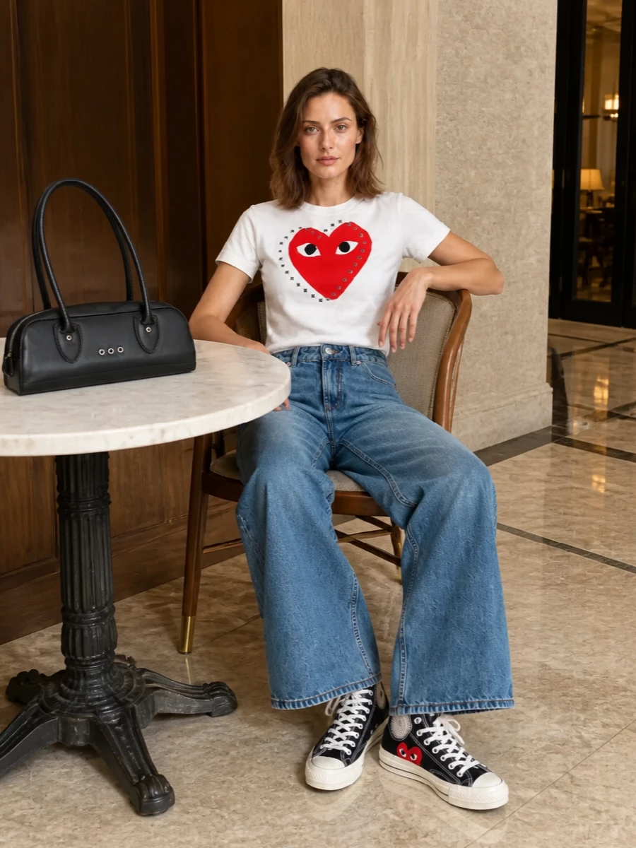 Graphic, heart-heavy Comme des Garçons Play energy meets soft, faded Ami denim for a relaxed streetwear take on preppy. The wide leg keeps everything easy and current, while black accents at the bag and sneakers sharpen the red-and-white tee instead of competing with it. It feels art-school casual yet considered, perfect for city days that stretch into low-key evenings.