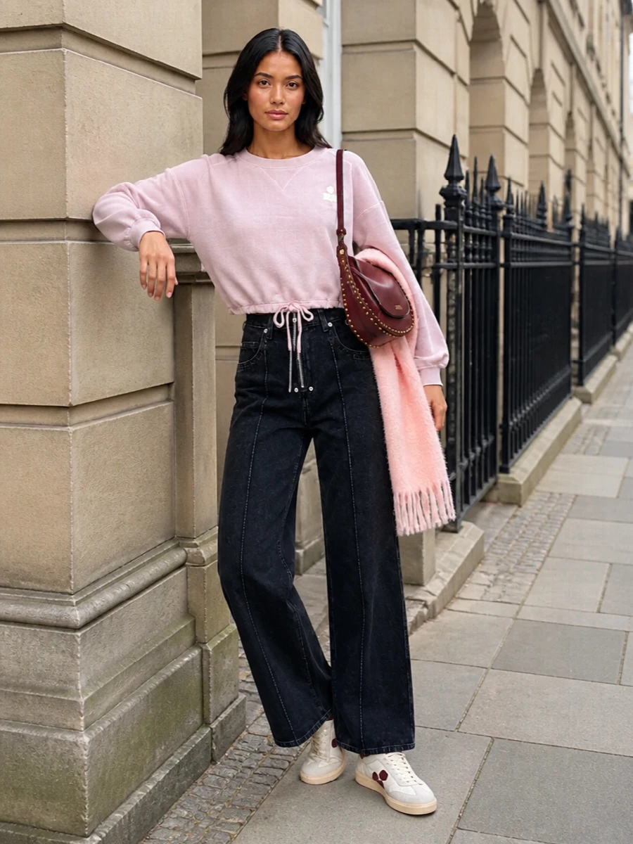 A blush cropped sweatshirt meets high-rise washed-black wide-leg denim for a relaxed, lengthening silhouette that still feels thought-through. Off-white court sneakers keep the palette light, while the burgundy crescent bag adds a single deep accent that reads quietly intentional. The soft blush scarf pulls the color story together and makes this an easy all-day city uniform for cooler months.
