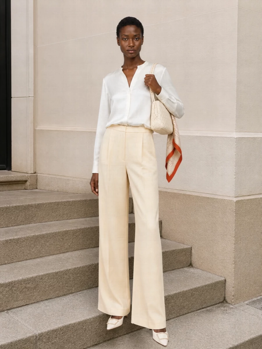 An ivory silk blouse and buttercream wide-leg trouser create a long, fluid column that feels relaxed yet boardroom ready. The pointed ivory pump and intrecciato bag refine the neutral palette while keeping the mood quiet and assured. A softly graphic scarf adds just enough detail to feel intentional without disturbing the calm lines.
