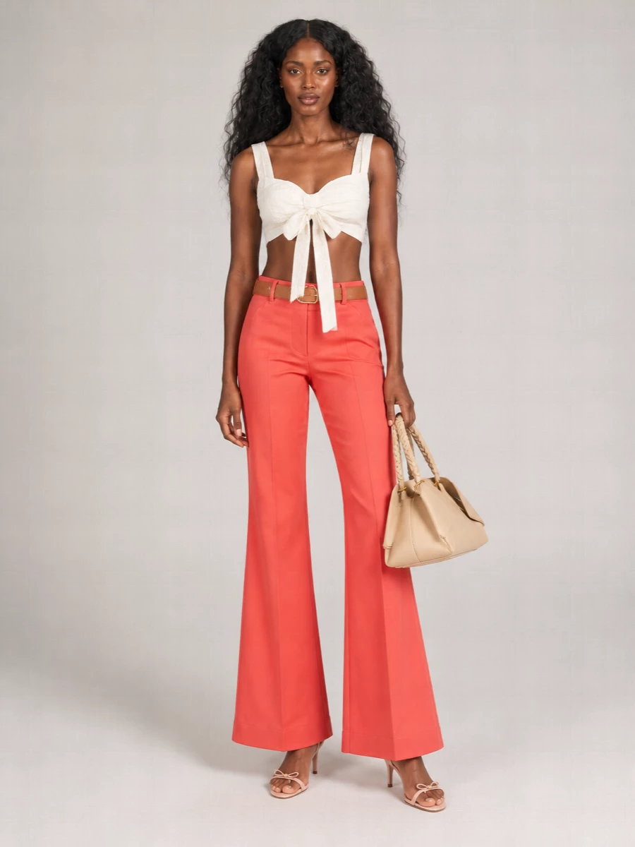 Sunlit coral tailoring meets sculpted white romance for a clean, modern take on boho dressing. The high-waisted flare and cropped tie-front top carve a long, fluid line, while nude sandals and a structured beige bag keep the focus on color and silhouette. A warm tan belt adds just enough definition at the waist for terrace lunches that stretch into late cocktails.