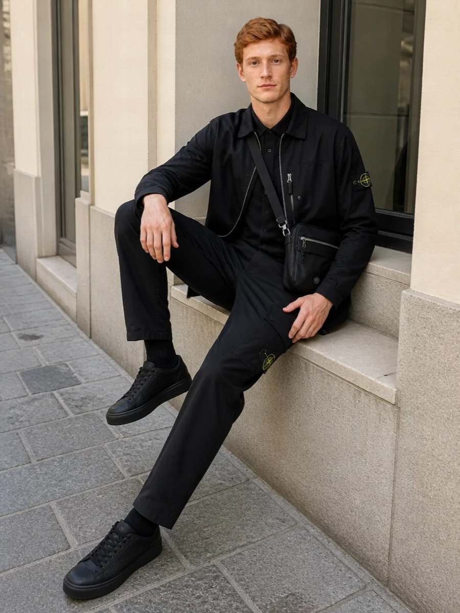 Head-to-toe Stone Island keeps this all-black, badge-driven setup tight and functional, with the coach-style shell over a boxy short-sleeve shirt for warm city days and nights. Straight cargos, technical runners and a compact crossbody keep the lines sharp and easy, letting fabric and hardware do the talking. It is a modular, urban uniform you can wear from commute to late bar without changing a piece.