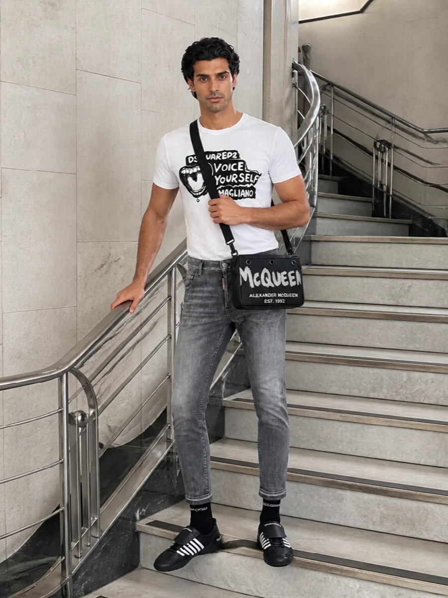 Monochrome graphics stay in focus with slim grey Dsquared2 denim that echoes the tee’s attitude without shouting. Black soccer-inspired sneakers keep the line clean and agile, while the McQueen crossbody and discreet logo socks add just enough detail for the city without breaking the graphic story.