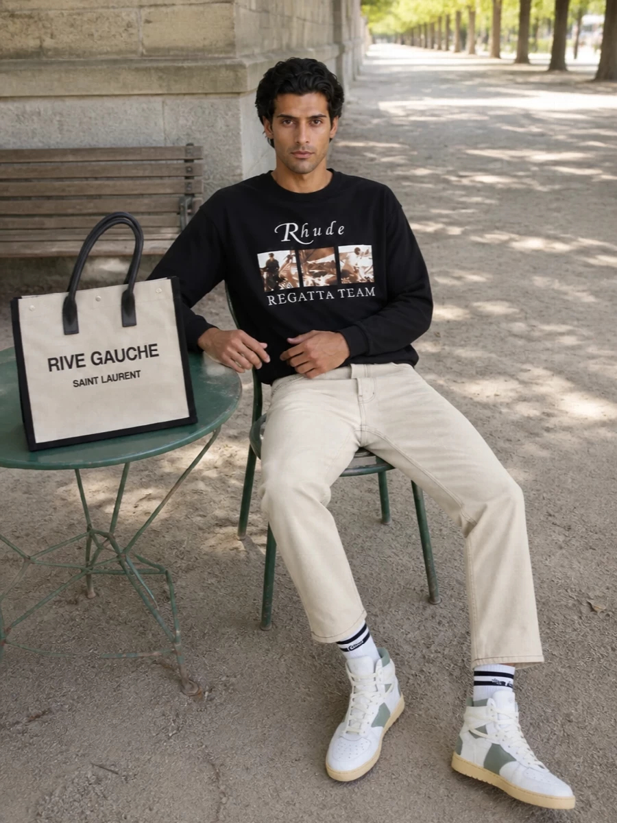A vintage regatta graphic top sits over washed light-beige denim for a relaxed, sun-faded base that feels more marina than sidewalk. Sage-accented high-tops and clean striped socks keep the energy firmly in the sport-street space, while the Rive Gauche tote adds a graphic, city-ready finish that still works for a coastal afternoon.