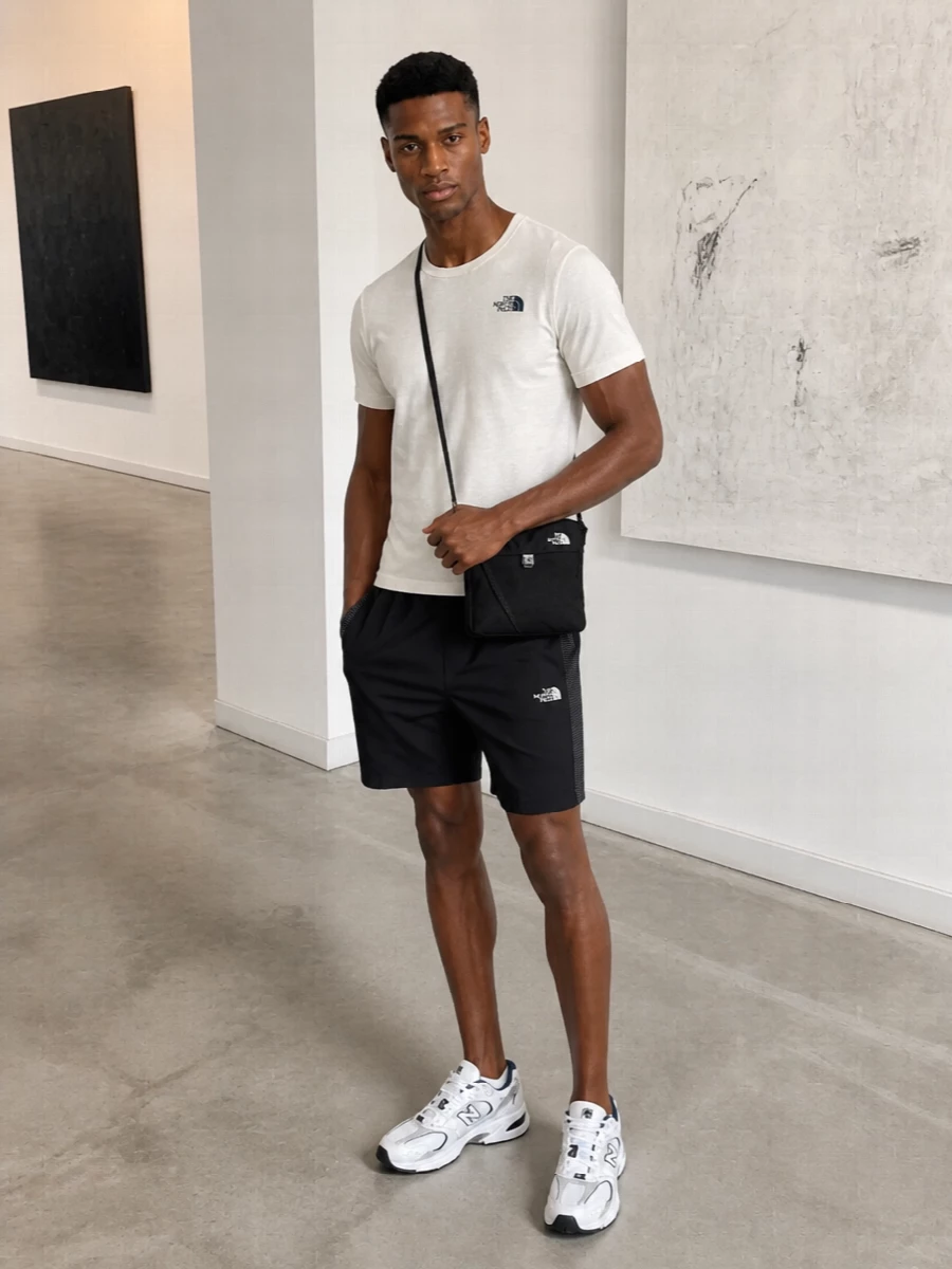 An off white and navy tee sits over clean black trail-inspired shorts for a simple sport-street uniform that works from city heat to weekend paths. White and navy runners echo the top without feeling matchy, while a compact black crossbody keeps your kit close and the silhouette streamlined. It is a low-key, technical take on warm weather dressing that still feels considered in every detail.