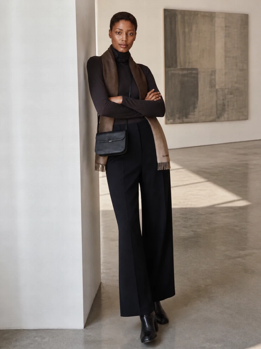 Charcoal brown and dense black sit together in a calm, elongated silhouette, with the sheer turtleneck softened by the fluid line of the wide-leg wool trouser. Sculptural black ankle boots and a slim crossbody keep the mood precise and quiet, while the ombré scarf introduces just enough warmth to stop the monochrome from feeling flat. It is a composed, minimalist uniform suited to long city days that quietly stretch into dinner.