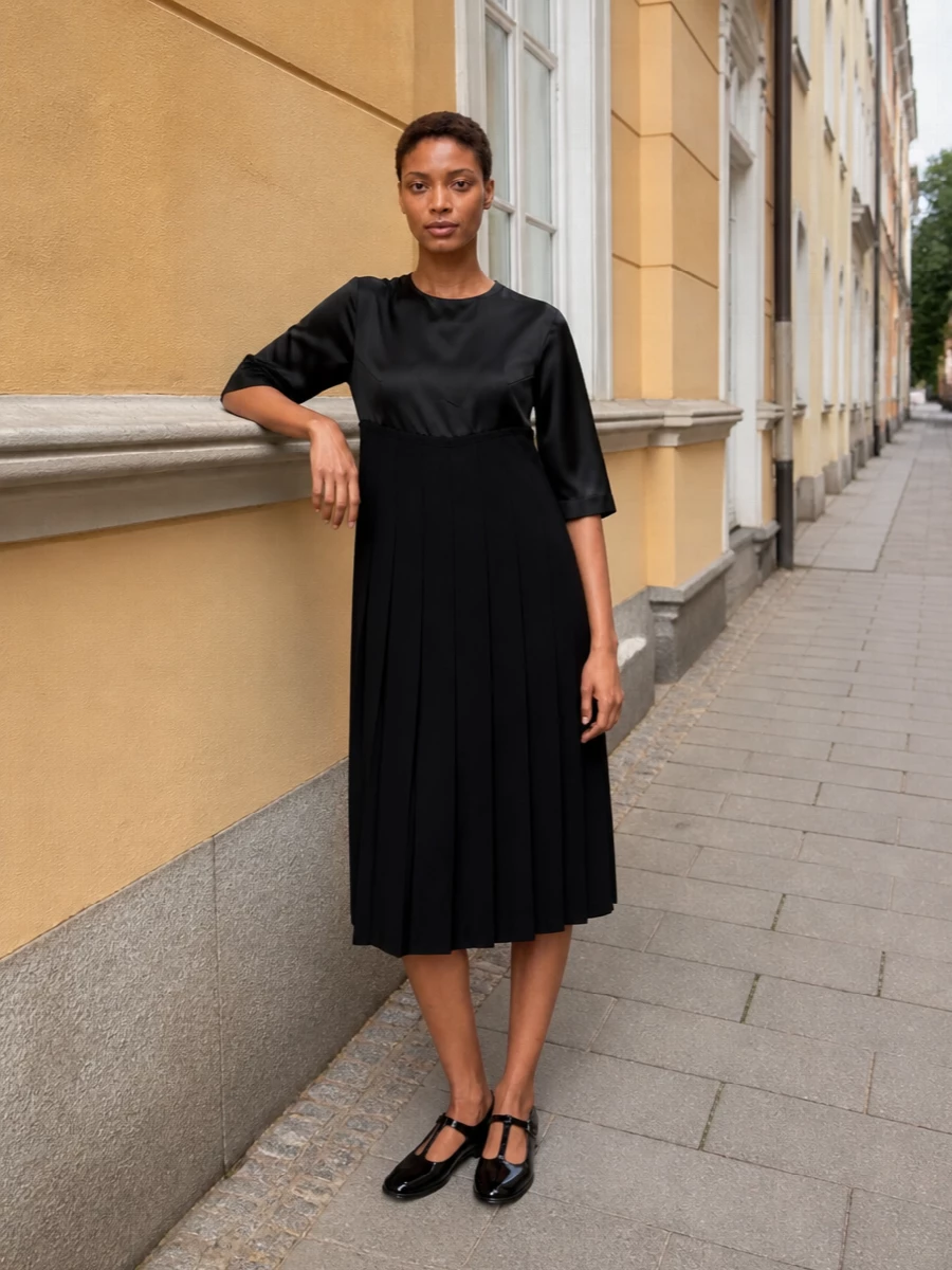 This is a rigorously black, sculptural ensemble that lets the Margiela Tabi Mary Janes feel intentional rather than quirky, echoing their quiet subversion through the pleated, satin-sliced dress. The mood is gallery opening or intimate dinner, with every line controlled and minimal, so the interest comes from cut, texture and proportion rather than hardware or color. Choosing the dress path over tailoring keeps the outfit clean and elongated, which works best with the split-toe flats’ refined, jewelry-like presence on the foot.