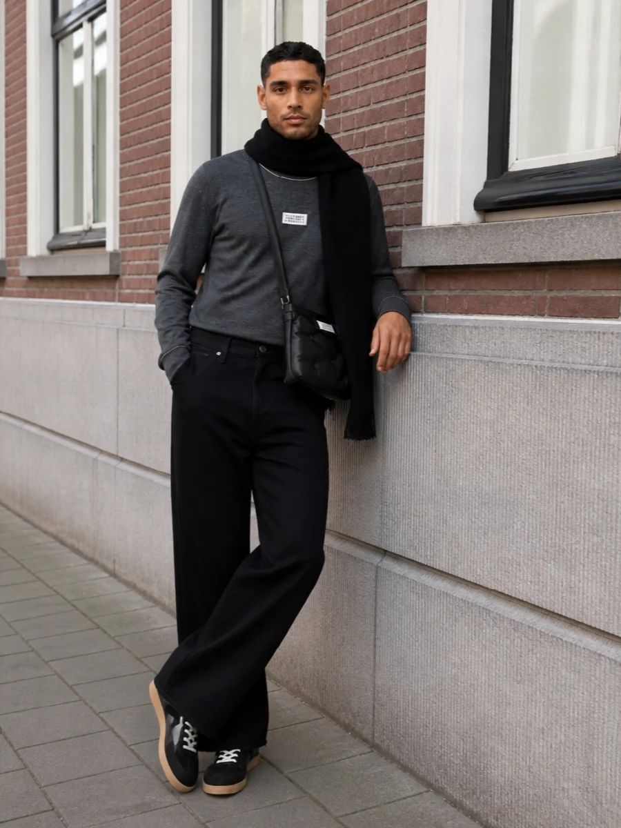 High-rise black wide-leg trousers meet a charcoal Margiela knit for a monochrome base that feels relaxed but precise. Charcoal and black sneakers keep the mood low-key and grounded, while a padded crossbody and stark black scarf introduce soft structure and texture without breaking the line.