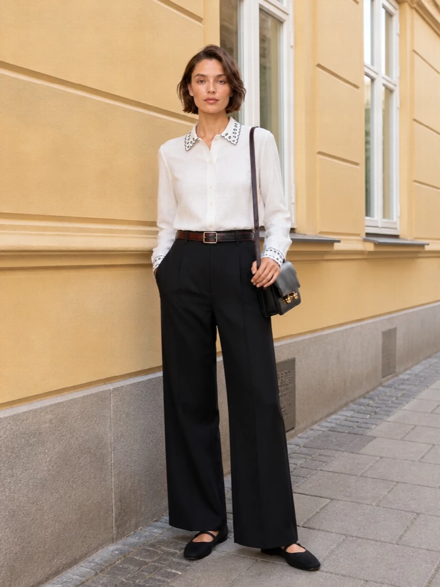 A crisp white Marni shirt with scalloped embroidery sits over high-rise black wide-leg trousers for a long, precise line that feels polished but not stiff. Black Mary Jane flats and a structured black shoulder bag keep the palette intentionally controlled, while the slim belt introduces a discreet graphic detail that nods to the shirt’s whimsy.