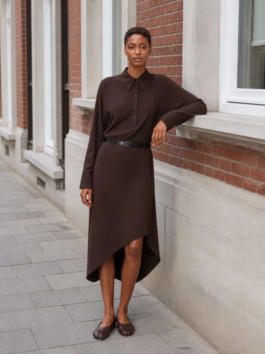 Deep chocolate and soft tailoring keep this outfit calm but intentional, with the asymmetric shirt dress and tabi flats speaking the same quiet, insider language. The single rich brown story reads modern and precise rather than matchy, and the scaled-up tote keeps the whole composition practical but composed. Choosing the dress path lets the sculpted hem and split toe remain the focus, instead of competing with separate tailoring lines.