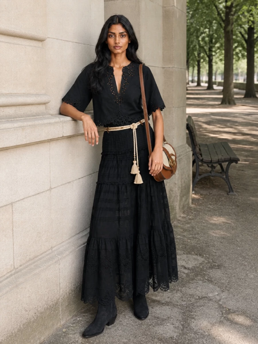 A black-on-black Marant pairing leans into romantic broderie and pleated tiers, creating a long, relaxed column with gentle movement. Inky Western boots and a tan raffia saddle bag keep it grounded yet soft, ideal for city days that drift into dinner. A braided rope belt adds a touch of boho texture and defines the waist without disturbing the ease of the silhouette.