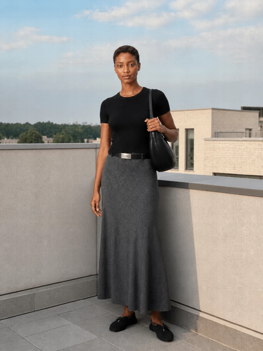 A finely knit black tee meets a charcoal cashmere maxi for a long, lean line that still feels soft and easy. Knitted flats keep it grounded and quiet, while a sculpted black shoulder bag and slim belt sharpen the proportions just enough for understated city days. The result is relaxed polish that moves naturally from coffee to a low-key dinner without changing a thing.